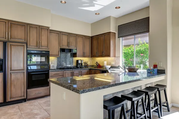 a kitchen with granite countertop a stove chairs and refrigerator
