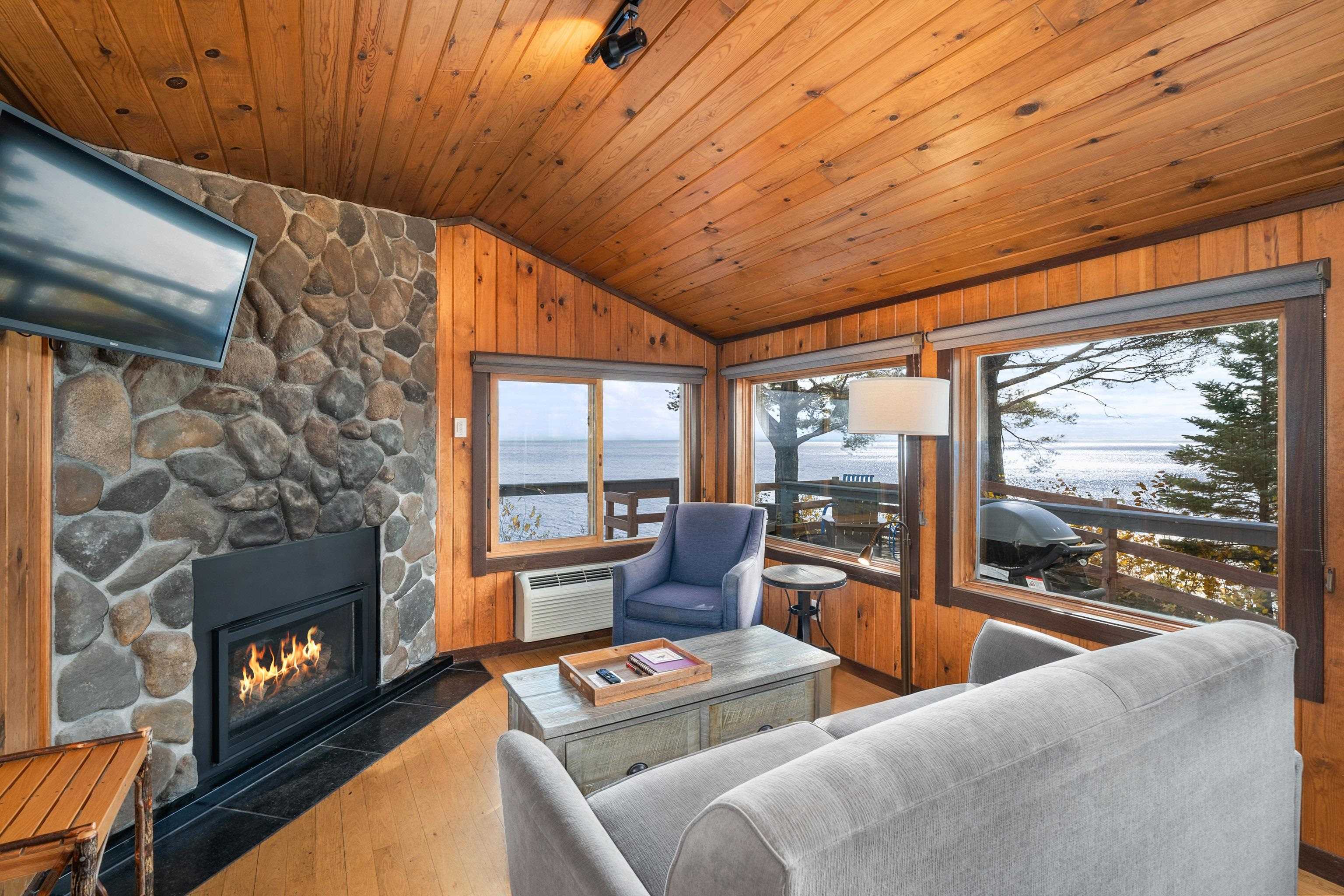Living area featuring vaulted ceiling, a stone fireplace, hardwood / wood-style floors, a water view, and wooden walls