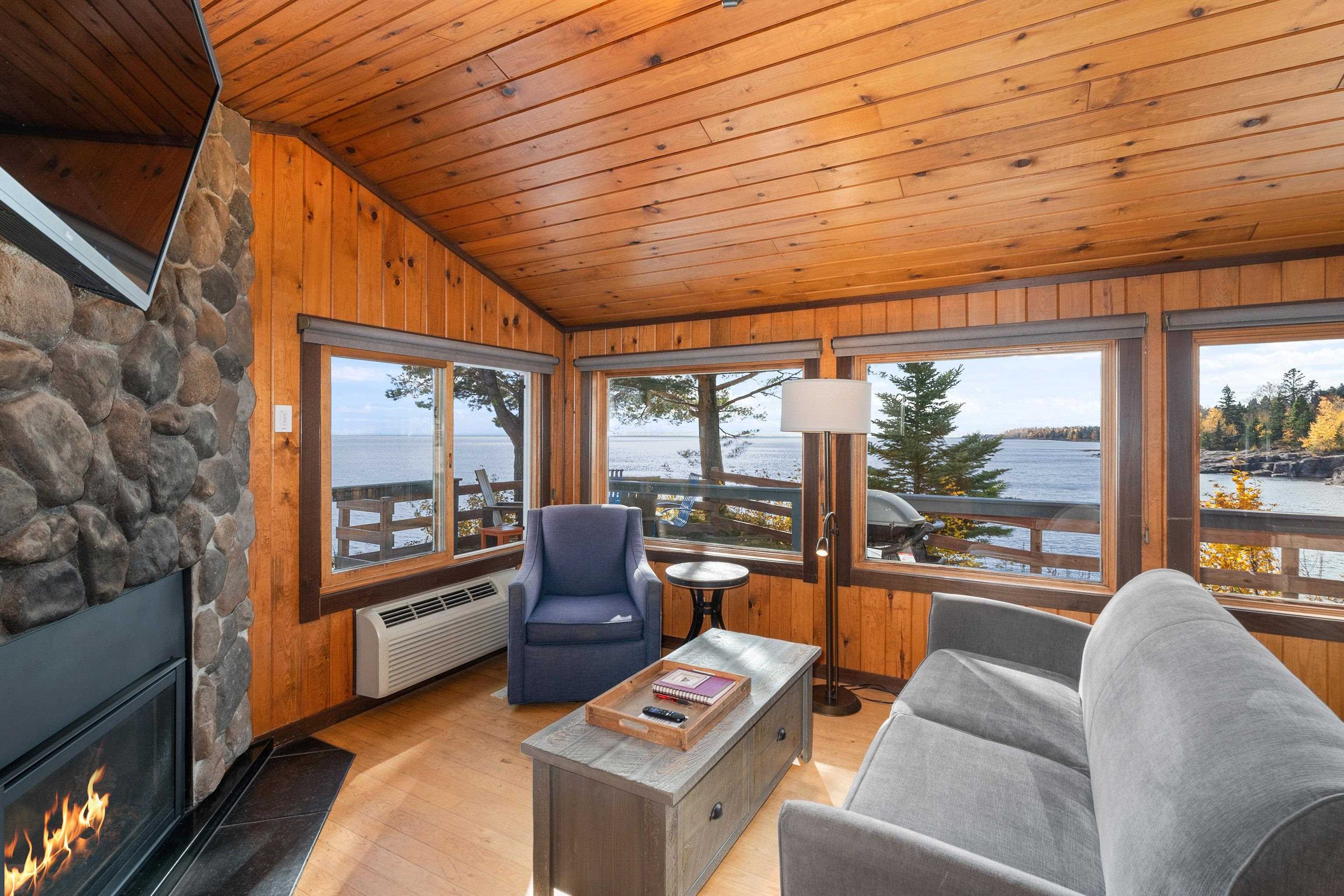 Living area with lofted ceiling, a water view, light wood-style floors, a stone fireplace, and wood ceiling