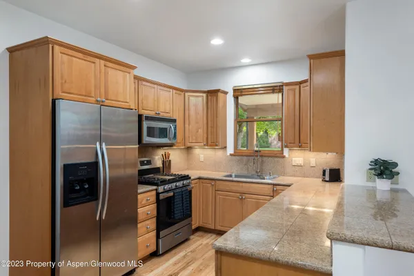 a kitchen with stainless steel appliances granite countertop a refrigerator a sink a stove a washer dryer and a dining table with wooden cabinet