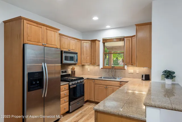 a kitchen with stainless steel appliances granite countertop a refrigerator a sink a stove a washer dryer and a dining table with wooden cabinet