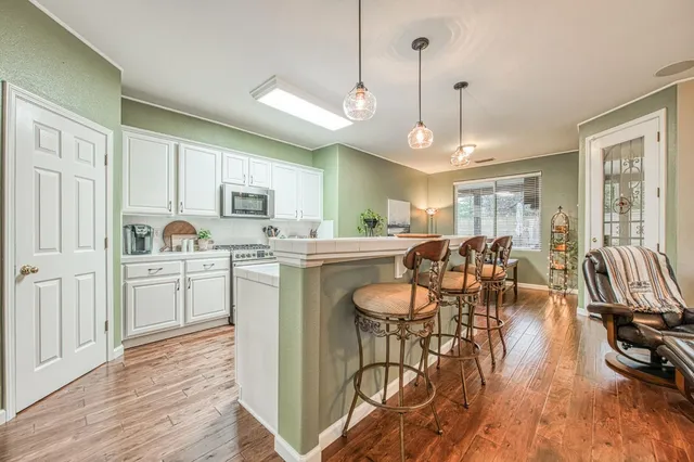 a kitchen with stainless steel appliances granite countertop a stove top oven a refrigerator a dining table and chairs with wooden floor