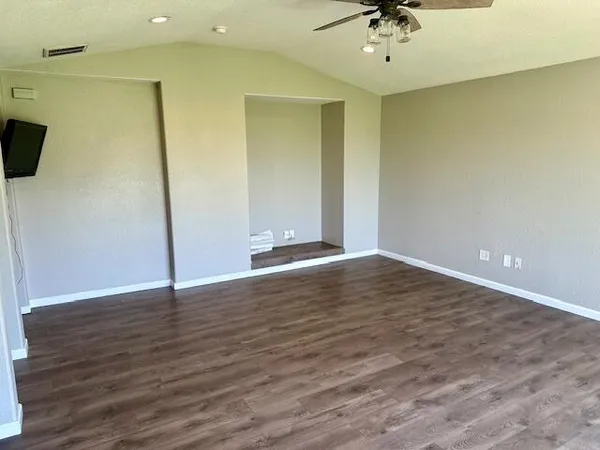 a view of an empty room with wooden floor and a ceiling fan