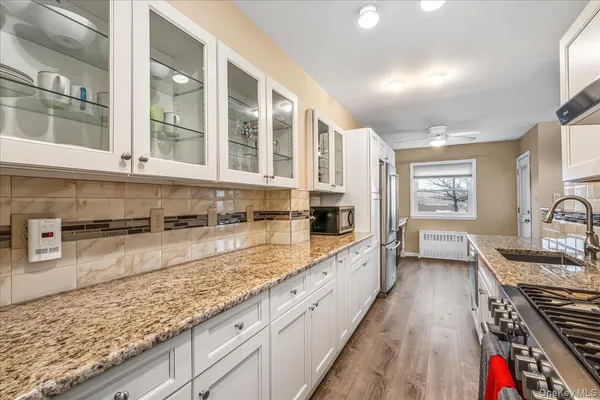 a large white kitchen with stainless steel appliances granite countertop a lot of counter space and wooden floors