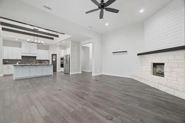 an empty room with wooden floor a ceiling fan and kitchen view