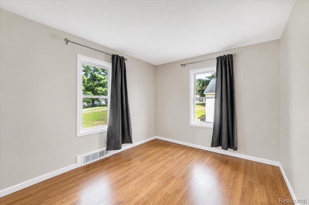 3852 North Lapeer Road Lapeer, MI 48446 - Photo 11 of 17 Bright room featuring wood-finish flooring, two windows with white trim, light gray walls, and white baseboards