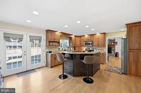 a kitchen with stainless steel appliances granite countertop a refrigerator a sink a stove and a dining table with wooden floor