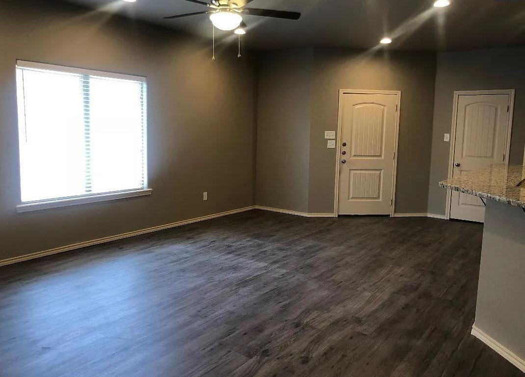 1203 Preston Trail, Unit B Wolfforth, TX 79382 - Photo 4 of 13 an empty room with wooden floor cabinet and windows