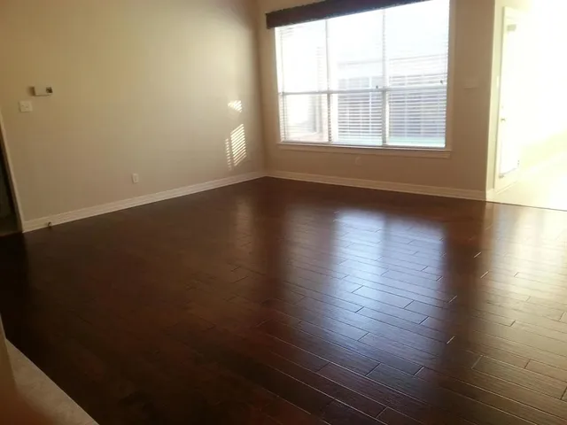 an empty room with wooden floor and windows with curtains