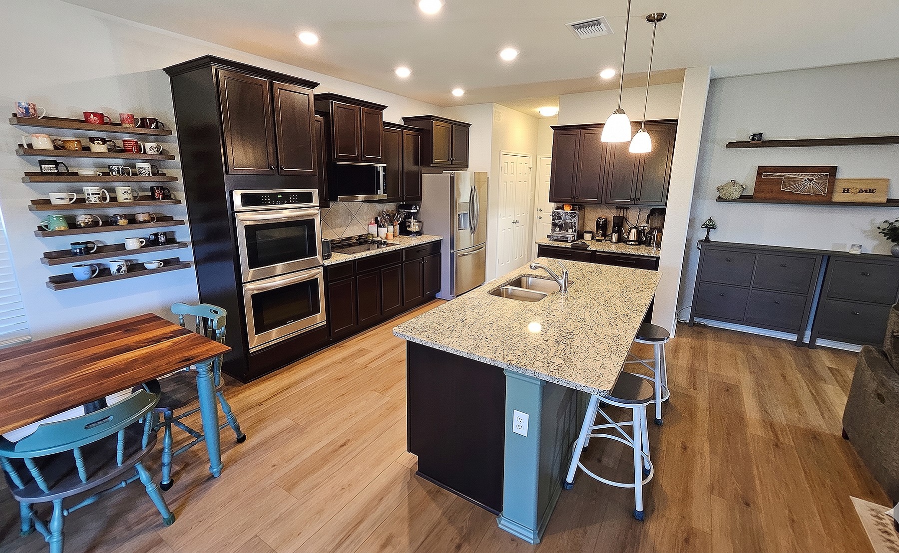 237 Bethann Drive Temple, TX 76502 - Photo 32 of 37 Open-concept kitchen featuring wood-finish flooring, dark wood cabinetry, a granite-topped island with an undermount double sink, stainless steel built-in double ovens, and recessed lighting