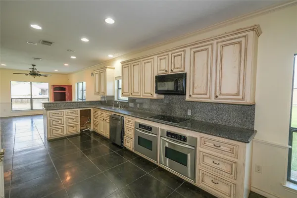 a large white kitchen with stainless steel appliances granite countertop a stove a sink a refrigerator and white cabinets with wooden floor