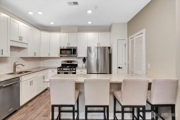 a kitchen with stainless steel appliances granite countertop a stove a sink a microwave a refrigerator and white cabinets