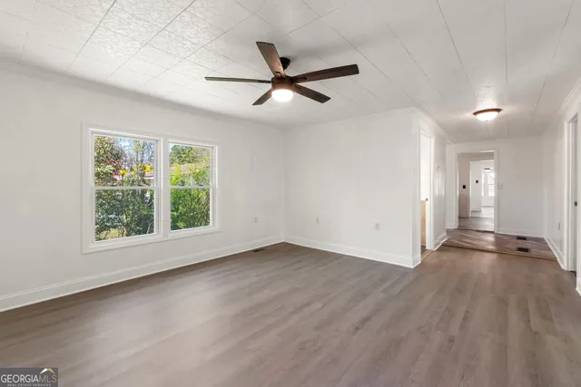 an empty room with wooden floor a ceiling fan and windows