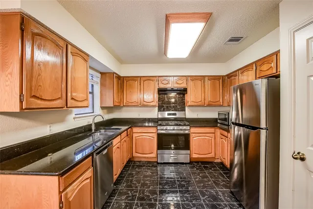a kitchen with stainless steel appliances granite countertop a refrigerator a stove and a sink