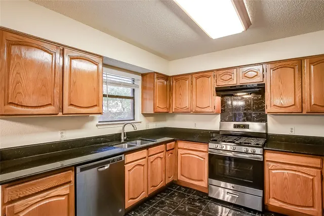 a kitchen with granite countertop a sink cabinets stainless steel appliances and a window