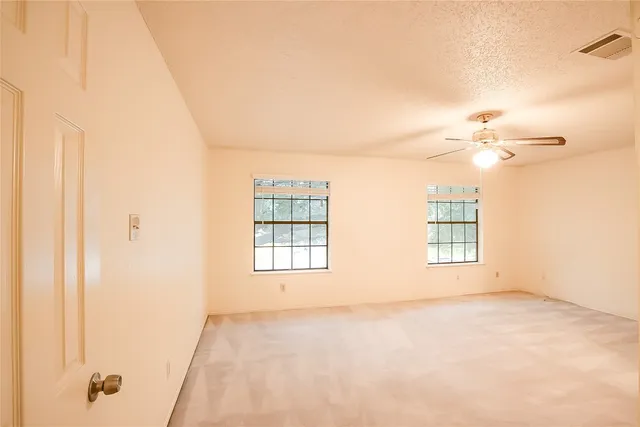 an empty room with a chandelier fan and windows