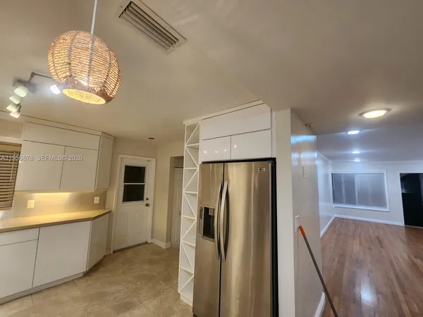 a view of a refrigerator in kitchen and an empty room with wooden floor