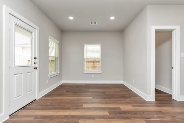 a view of an empty room with wooden floor and a window