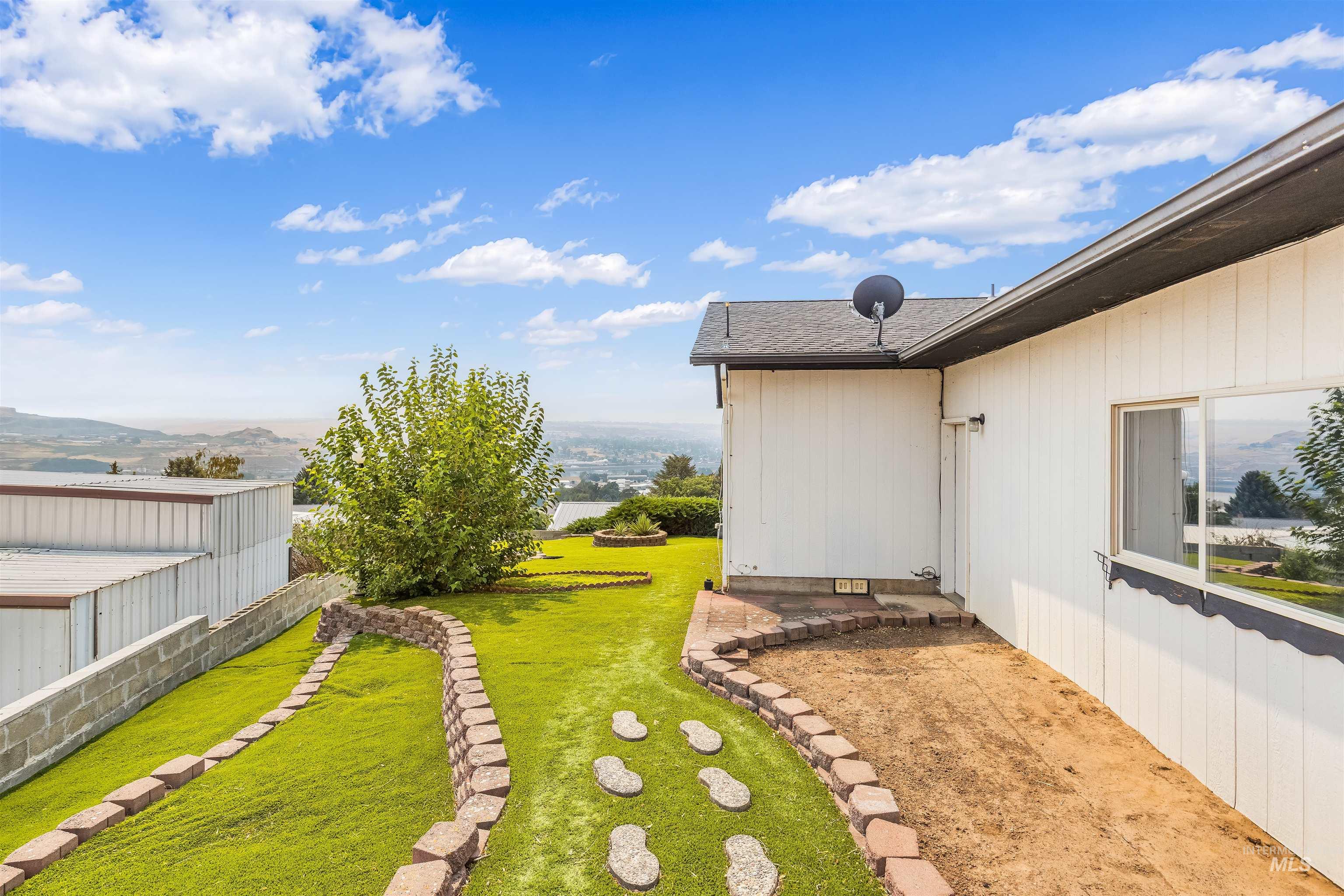 1133 Harvest Road Lewiston, ID 83501 - Photo 11 of 45 Expansive backyard oasis featuring a meticulously manicured lawn, mature landscaping with established trees, decorative stone pathway, and defined planting beds