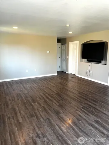 a view of an empty room with wooden floor and a kitchen