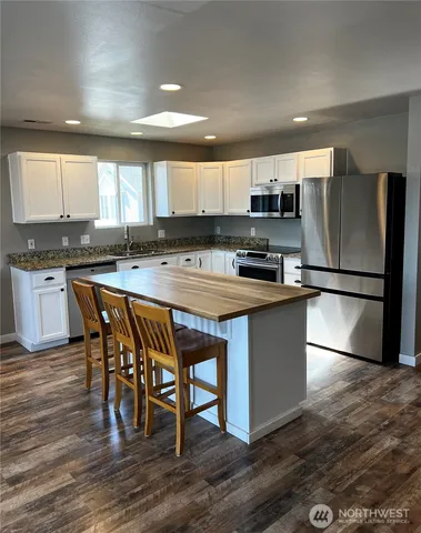 a kitchen with stainless steel appliances granite countertop a stove a sink a microwave a refrigerator white cabinets and wooden floor