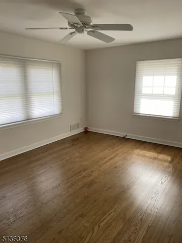 an empty room with wooden floor fan and windows