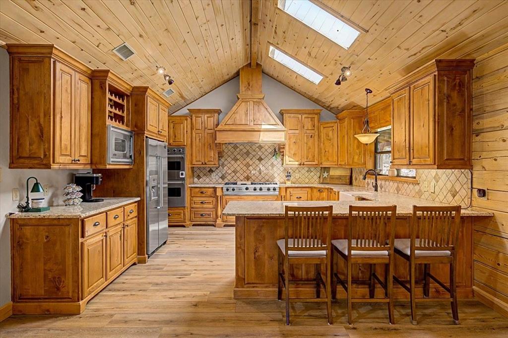 Kitchen featuring vaulted wood-plank ceilings with skylights, extensive wood cabinetry, wood-finish flooring, and a tile backsplash