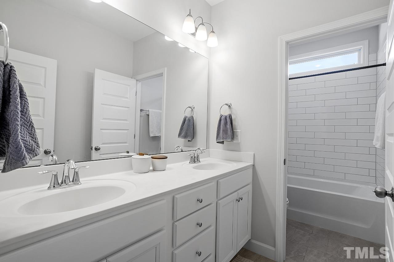1445 Commons Ford Place Apex, NC 27539 - Photo 27 of 34 a bathroom with a double vanity sink a mirror and a bathtub