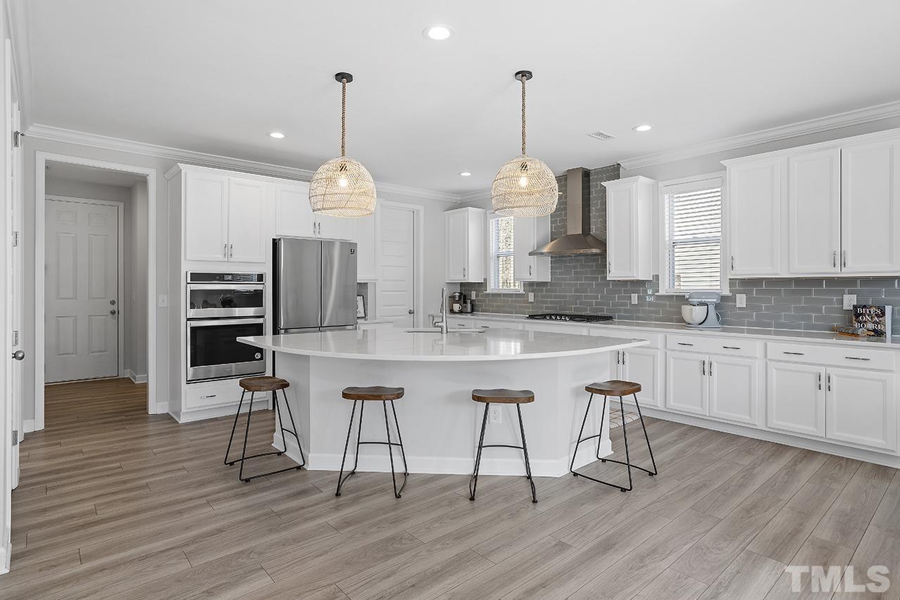 1445 Commons Ford Place Apex, NC 27539 - Photo 3 of 34 a kitchen with stainless steel appliances granite countertop a stove a sink dishwasher a refrigerator and white cabinets with wooden floor