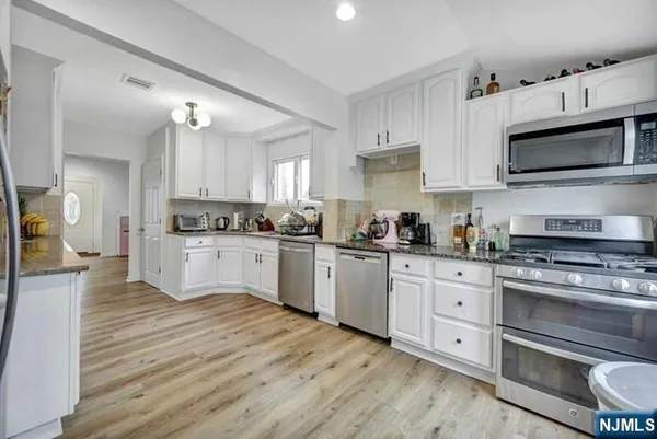 a kitchen with stainless steel appliances white cabinets a sink a stove a microwave and wooden floors