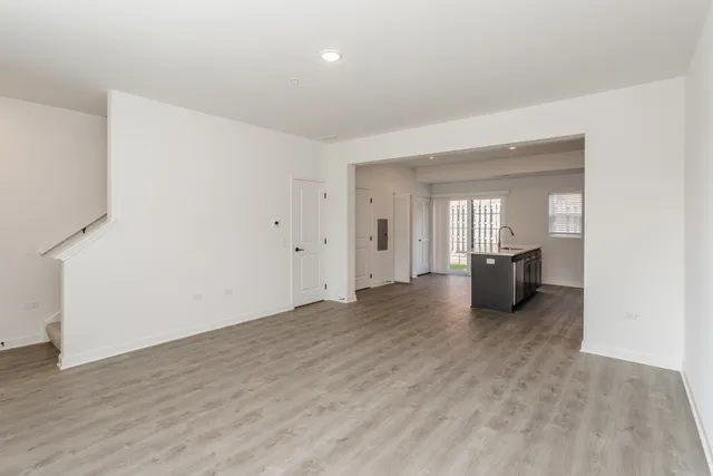 a view of an empty room with wooden floor and a kitchen