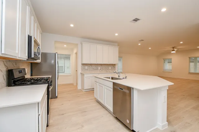 a kitchen with stainless steel appliances a sink a stove a refrigerator cabinets and a window