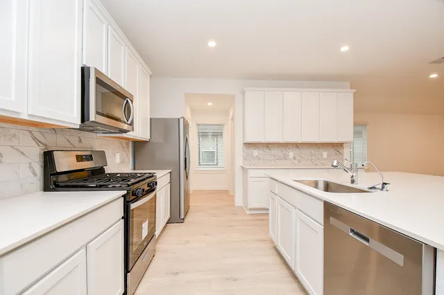 a view of an empty room with kitchen appliances and a ceiling fan