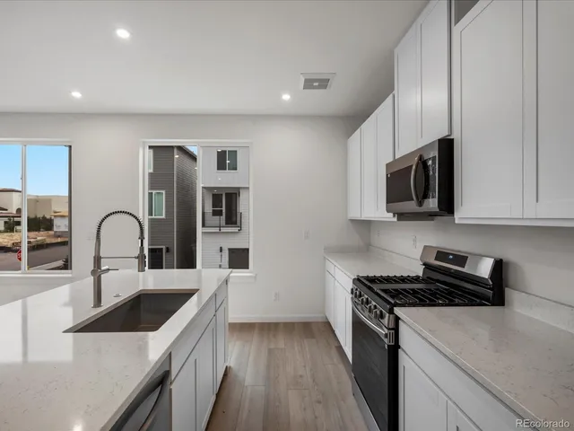 a kitchen with stainless steel appliances granite countertop a sink a stove top oven a refrigerator with wooden cabinets and floor