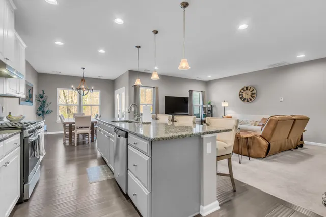 a kitchen with stainless steel appliances granite countertop a stove top oven a sink dishwasher a dining table and chairs with wooden floor