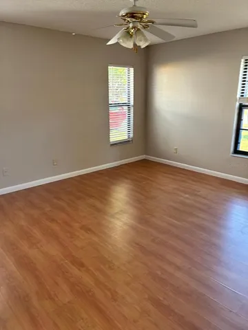 an empty room with wooden floor chandelier fan and windows