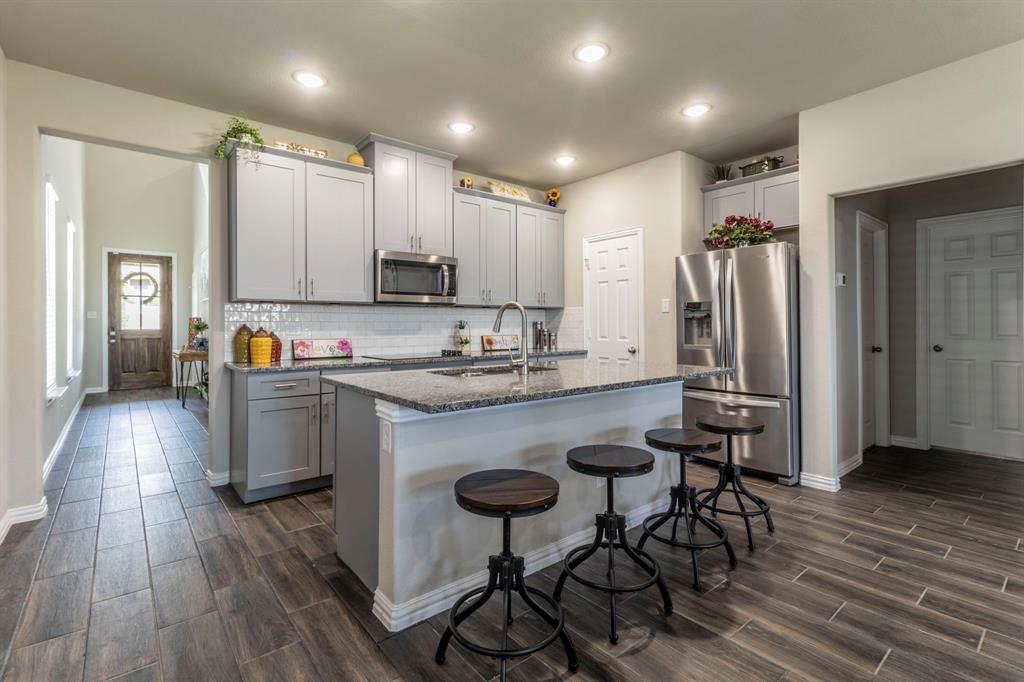626 Ruthye Lane Pilot Point, TX 76258 - Photo 3 of 27 Kitchen with stainless steel appliances, gray cabinetry, dark stone countertops, a kitchen bar, and a center island with sink
