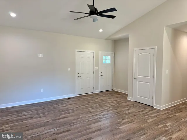 an empty room with wooden floor a ceiling fan and windows