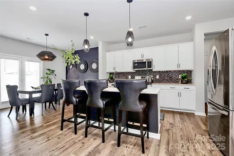 a kitchen with stainless steel appliances granite countertop a stove a refrigerator a microwave a dining table and chairs with wooden floor