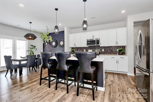 a kitchen with stainless steel appliances granite countertop a stove a refrigerator a microwave a dining table and chairs with wooden floor