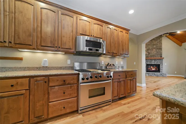 a kitchen with stainless steel appliances granite countertop a refrigerator a sink dishwasher and a fireplace with wooden floor