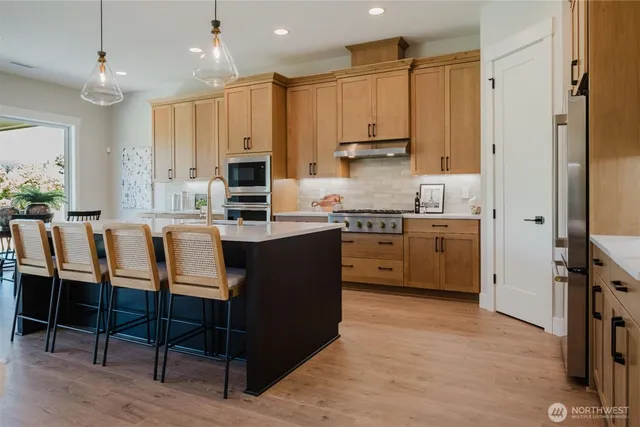 a kitchen with stainless steel appliances granite countertop a stove top oven a sink dishwasher and a refrigerator with wooden floor