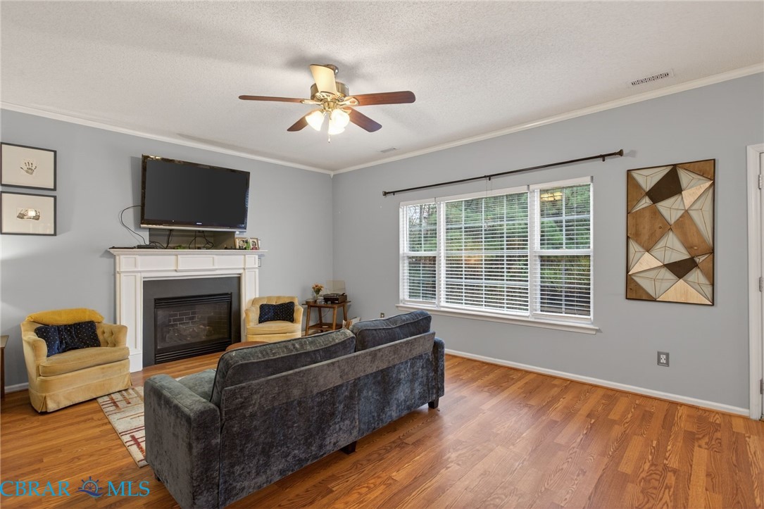 116 Old Field Road Williamsburg, VA 23188 - Photo 6 of 27 Living room with a glass covered fireplace, wood finished floors, crown molding, a textured ceiling, and ceiling fan