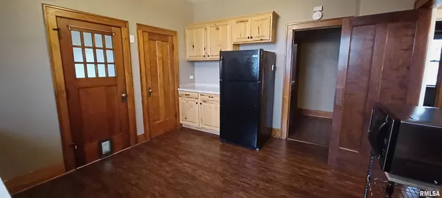 a view of a refrigerator in kitchen and an empty room with wooden floor