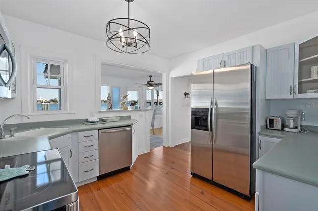 a kitchen with stainless steel appliances granite countertop a refrigerator a sink dishwasher a stove and white cabinets with wooden floor