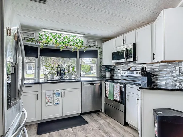 a kitchen with stainless steel appliances granite countertop a refrigerator a sink dishwasher and white cabinets with wooden floor