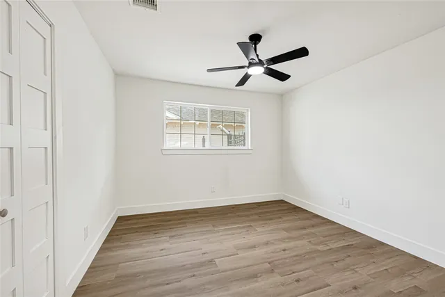 an empty room with wooden floor fan and windows