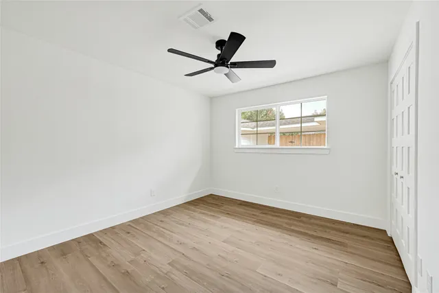 an empty room with wooden floor ceiling fan and windows