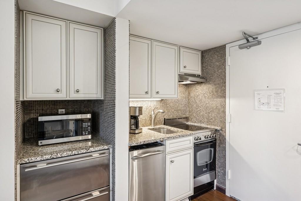 236 Edgemere Street, Unit 427 Montauk, NY 11954 - Photo 5 of 42 Kitchen with decorative backsplash, appliances with stainless steel finishes, light stone counters, white cabinets, and dark wood-type flooring