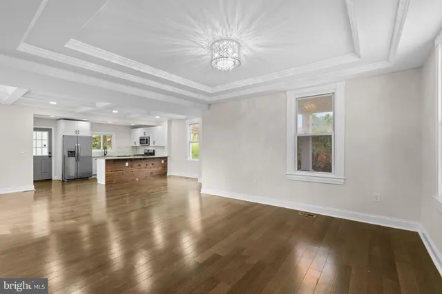 a view of an empty room with wooden floor and a kitchen